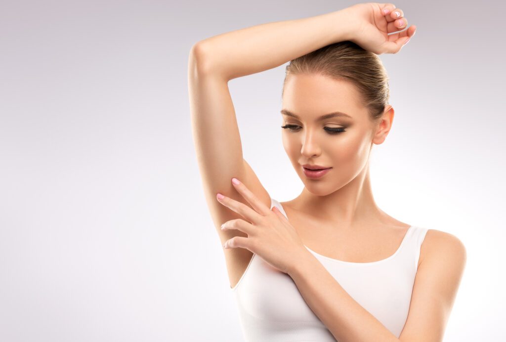 Young, woman dressed in sport bra is touching clean, soft skin of armpit. Beauty, cosmetology and skin care.